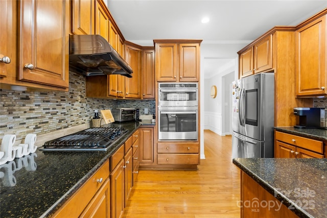 kitchen featuring decorative backsplash, dark stone counters, exhaust hood, light hardwood / wood-style floors, and stainless steel appliances