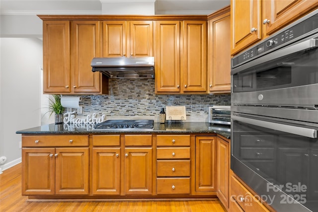 kitchen featuring dark stone countertops, appliances with stainless steel finishes, range hood, light hardwood / wood-style floors, and decorative backsplash