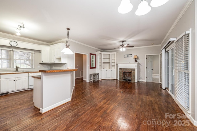 kitchen with butcher block countertops, white cabinetry, decorative light fixtures, dishwasher, and a tiled fireplace