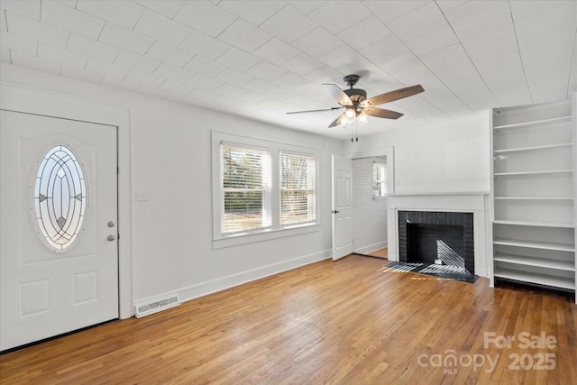 unfurnished living room featuring built in shelves, ceiling fan, a fireplace, and hardwood / wood-style floors