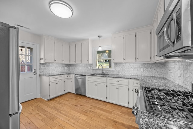 kitchen with sink, decorative light fixtures, stainless steel appliances, light stone countertops, and white cabinets