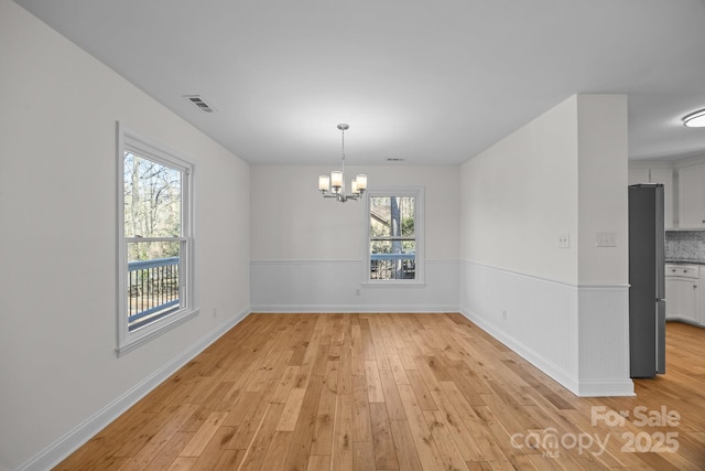 unfurnished dining area with an inviting chandelier and light hardwood / wood-style flooring