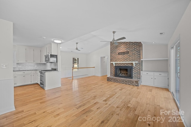 unfurnished living room featuring ceiling fan, a fireplace, vaulted ceiling, and light hardwood / wood-style flooring