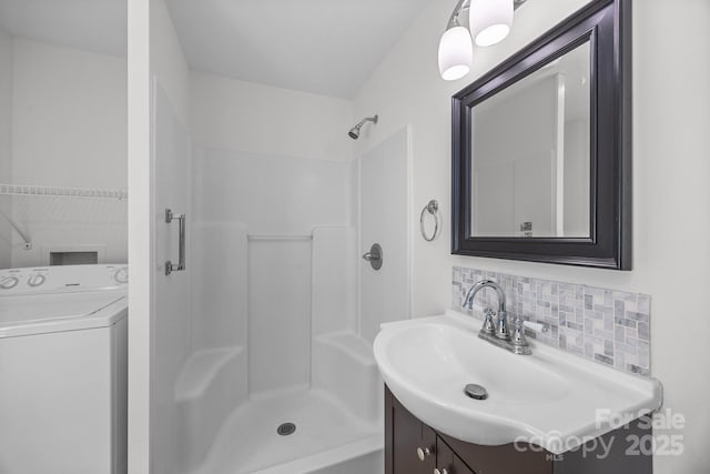 bathroom featuring vanity, washer / dryer, a shower, and backsplash