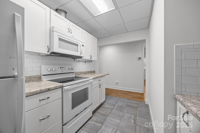 kitchen with tasteful backsplash, a paneled ceiling, white cabinets, and white appliances