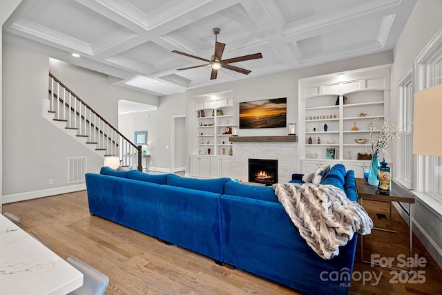 living room featuring hardwood / wood-style flooring, coffered ceiling, a fireplace, built in shelves, and beamed ceiling