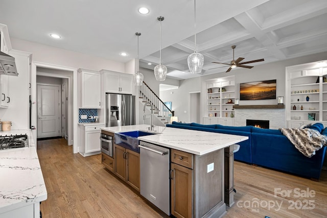 kitchen with white cabinetry, appliances with stainless steel finishes, an island with sink, and light stone counters