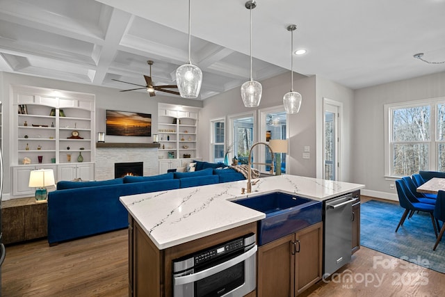 kitchen featuring sink, dark wood-type flooring, hanging light fixtures, a fireplace, and a center island with sink