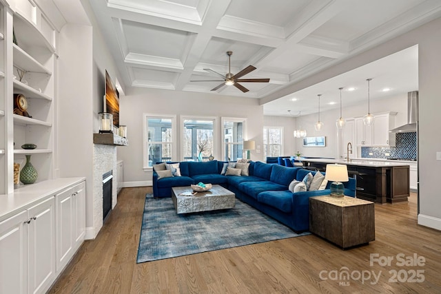 living room with ceiling fan, coffered ceiling, a stone fireplace, beamed ceiling, and light wood-type flooring