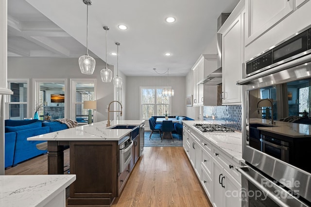 kitchen with sink, white cabinetry, appliances with stainless steel finishes, pendant lighting, and a kitchen island with sink