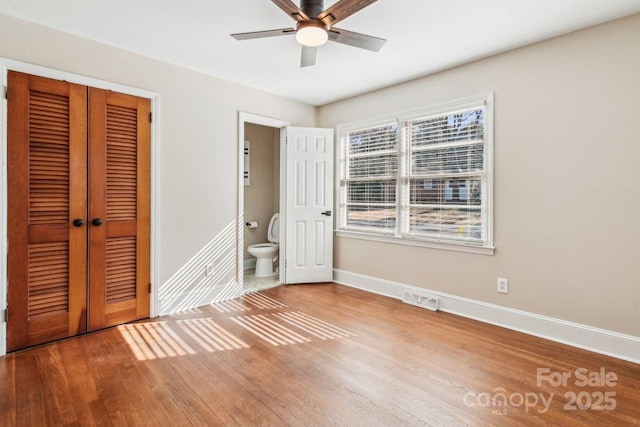 unfurnished bedroom featuring connected bathroom, hardwood / wood-style floors, ceiling fan, and a closet