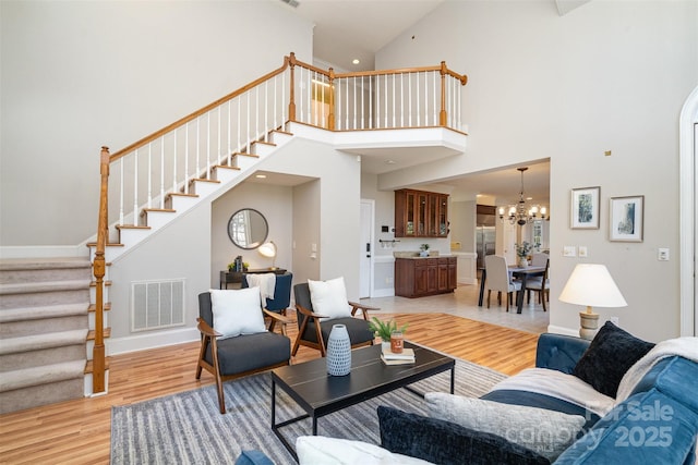 living room with a towering ceiling, an inviting chandelier, and light hardwood / wood-style flooring