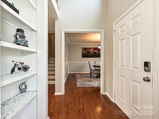 corridor with built in shelves, dark wood-type flooring, and ornamental molding