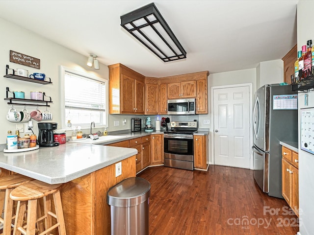 kitchen featuring sink, a breakfast bar area, appliances with stainless steel finishes, dark hardwood / wood-style floors, and kitchen peninsula