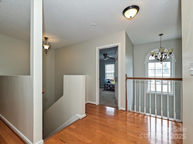 corridor with hardwood / wood-style floors, a notable chandelier, and a textured ceiling