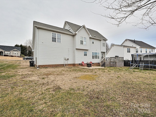 rear view of house featuring a wooden deck, a yard, and a trampoline