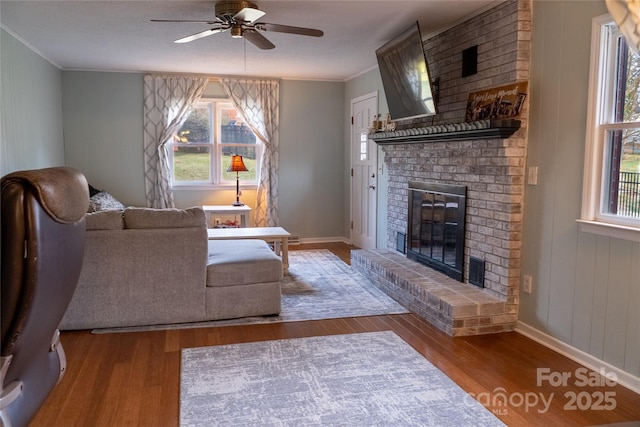 living room with ornamental molding, ceiling fan, a fireplace, and light wood-type flooring