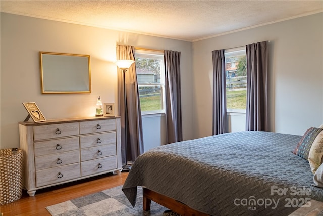 bedroom with a textured ceiling, ornamental molding, and wood finished floors