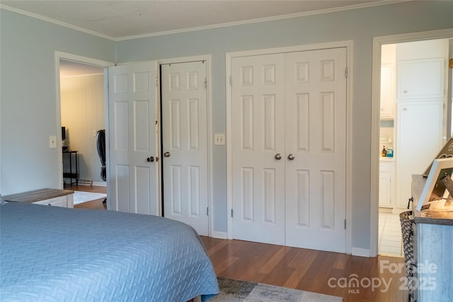 bedroom featuring baseboards, ornamental molding, multiple closets, and wood finished floors