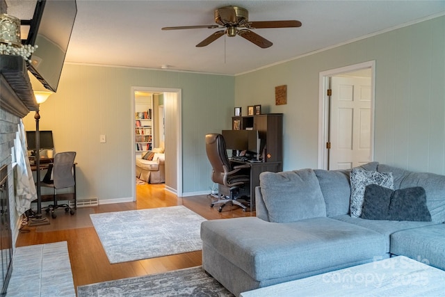 living area with crown molding, ceiling fan, baseboards, a fireplace with flush hearth, and wood finished floors