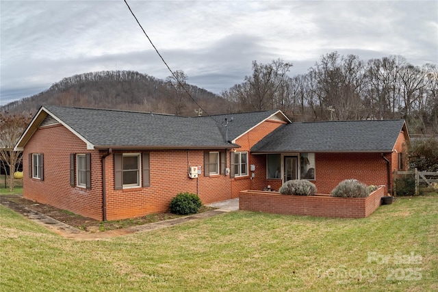 back of property with roof with shingles, a mountain view, a yard, and brick siding
