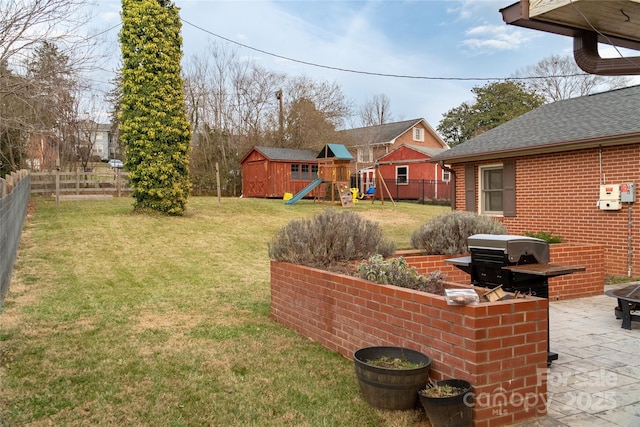 view of yard with fence, an outdoor structure, a shed, a playground, and a patio
