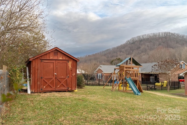 view of jungle gym with an outdoor structure, fence, a storage unit, a lawn, and a mountain view