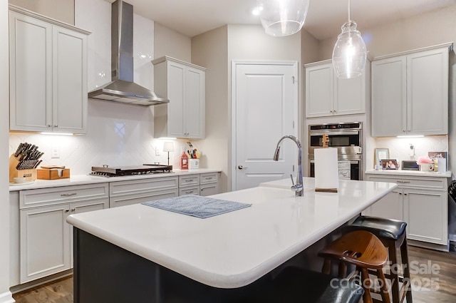 kitchen featuring wall chimney range hood, stainless steel appliances, and a kitchen island with sink