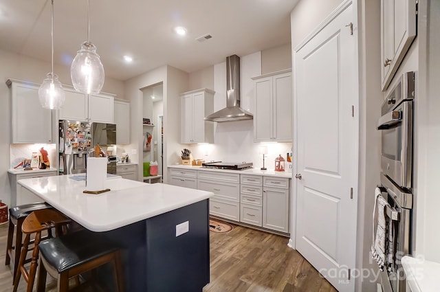 kitchen with hanging light fixtures, a kitchen breakfast bar, stainless steel appliances, wall chimney range hood, and a center island