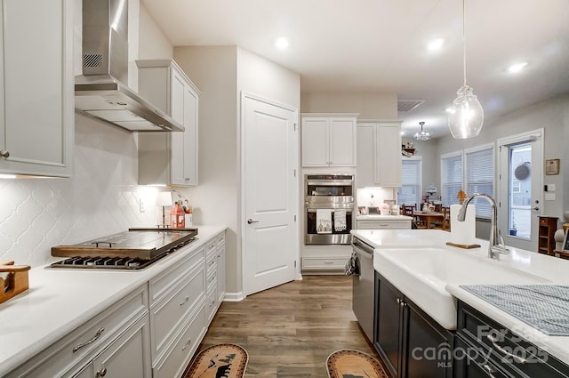 kitchen featuring wall chimney range hood, pendant lighting, white cabinetry, and appliances with stainless steel finishes