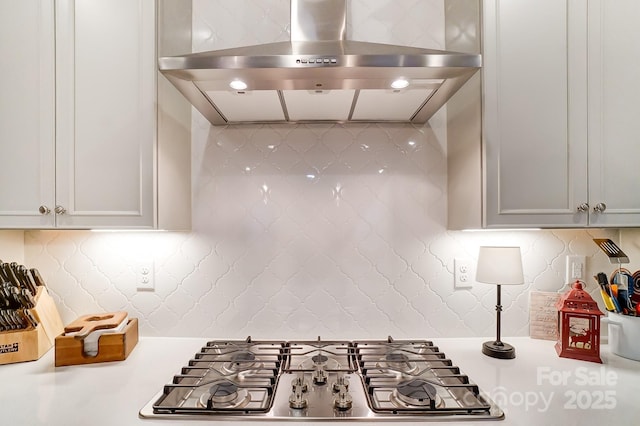 kitchen with stainless steel gas stovetop, tasteful backsplash, white cabinets, and range hood