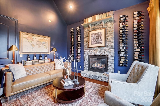 living room featuring vaulted ceiling, a stone fireplace, and wood-type flooring