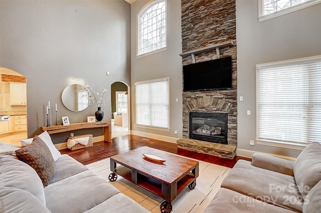 living room featuring a fireplace, light hardwood / wood-style floors, a healthy amount of sunlight, and a high ceiling