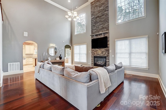 living room featuring ornamental molding, dark hardwood / wood-style floors, a stone fireplace, and a wealth of natural light