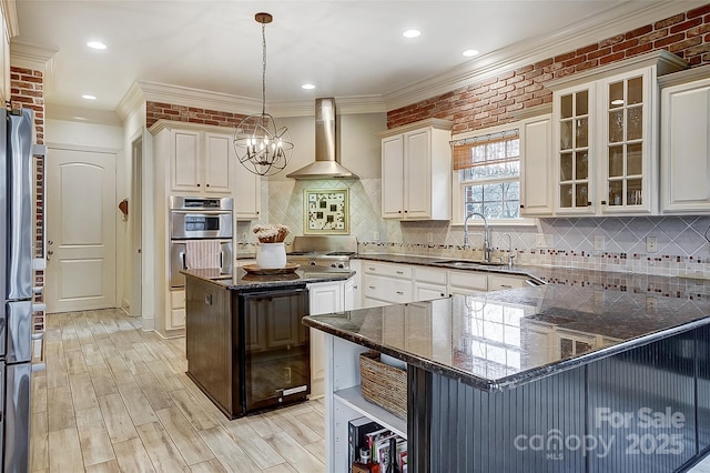 kitchen featuring wall chimney exhaust hood, sink, hanging light fixtures, stainless steel appliances, and white cabinets