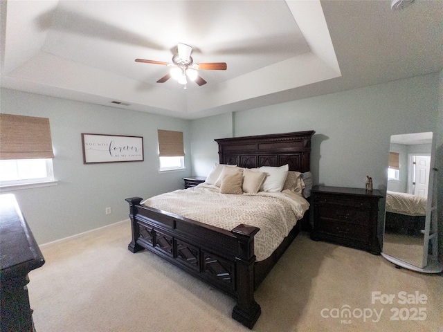 carpeted bedroom with a raised ceiling and ceiling fan