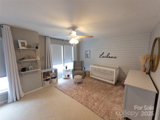 bedroom featuring a nursery area, ceiling fan, and carpet flooring