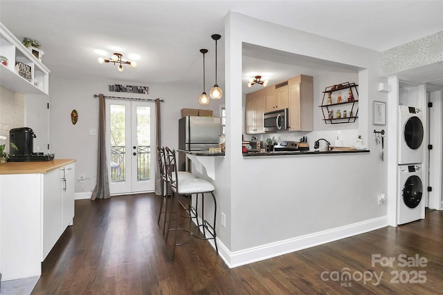 kitchen with french doors, stacked washer and dryer, decorative light fixtures, appliances with stainless steel finishes, and dark hardwood / wood-style floors