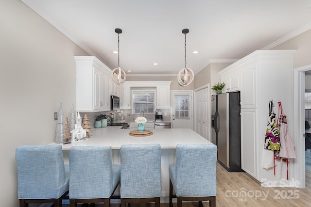 kitchen featuring white cabinetry, hanging light fixtures, a kitchen breakfast bar, stainless steel appliances, and kitchen peninsula