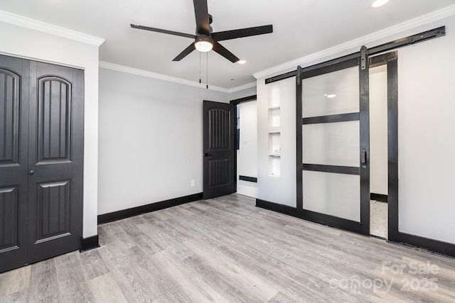 unfurnished bedroom featuring crown molding, light hardwood / wood-style floors, a barn door, and ceiling fan