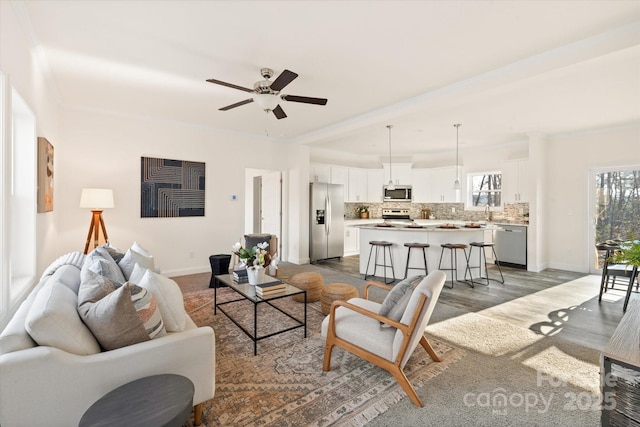 living room featuring crown molding, wood finished floors, baseboards, and ceiling fan