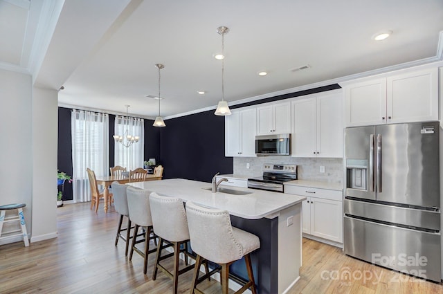 kitchen with an island with sink, white cabinetry, sink, hanging light fixtures, and stainless steel appliances