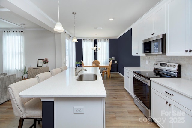 kitchen with appliances with stainless steel finishes, pendant lighting, sink, white cabinets, and a center island with sink