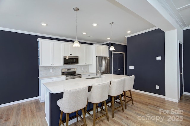 kitchen featuring appliances with stainless steel finishes, decorative light fixtures, white cabinetry, sink, and a center island with sink