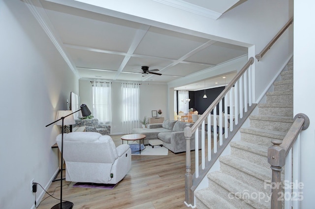 living room with ceiling fan, ornamental molding, coffered ceiling, and light wood-type flooring