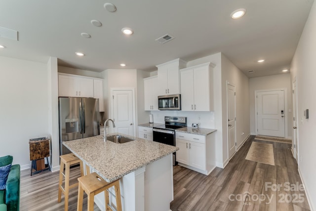 kitchen featuring appliances with stainless steel finishes, white cabinetry, sink, a kitchen breakfast bar, and a center island with sink