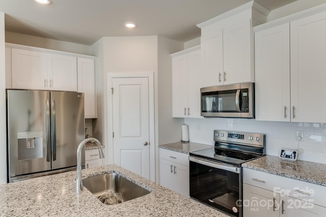 kitchen featuring light stone countertops, white cabinetry, appliances with stainless steel finishes, and sink