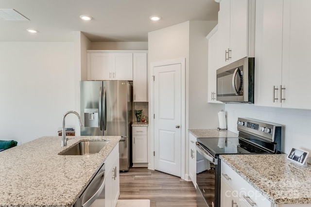 kitchen featuring stainless steel appliances, white cabinetry, a center island with sink, and light stone counters