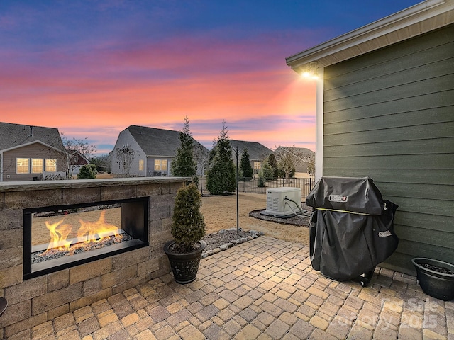 patio terrace at dusk featuring exterior fireplace and a grill