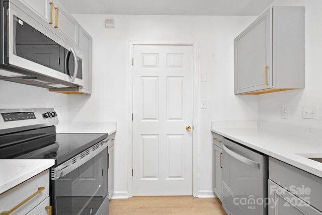 kitchen featuring light stone countertops, appliances with stainless steel finishes, gray cabinetry, and light hardwood / wood-style floors